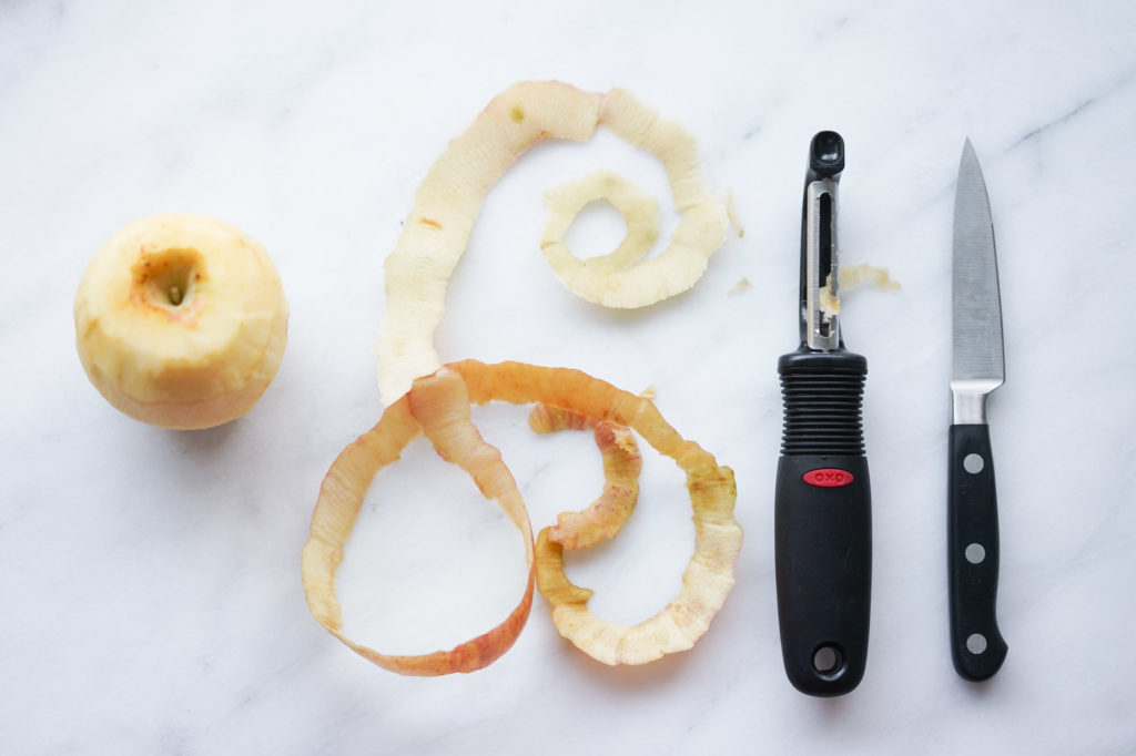 a peeled apple, next to a peeler, and paring knife